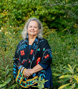 Robin Kimmerer standing surrounded by plants